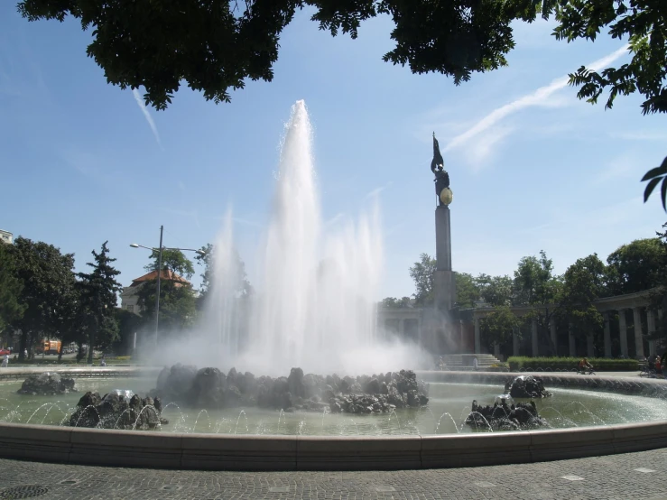 water fountain next to a monument and trees in a park