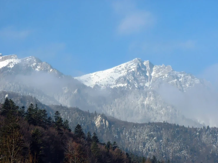 a mountain covered in snow and clouds under blue sky