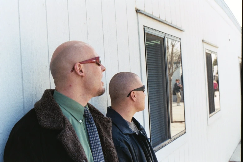 two bald guys standing in front of the window
