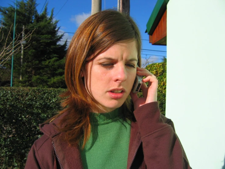 woman is on her cell phone outside, with a green shirt and purple sweatshirt