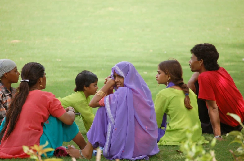 a group of children sitting in a field with one child touching their face