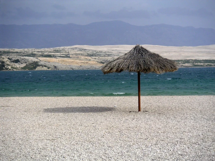 a straw umbrella is sitting on a beach with water in the background