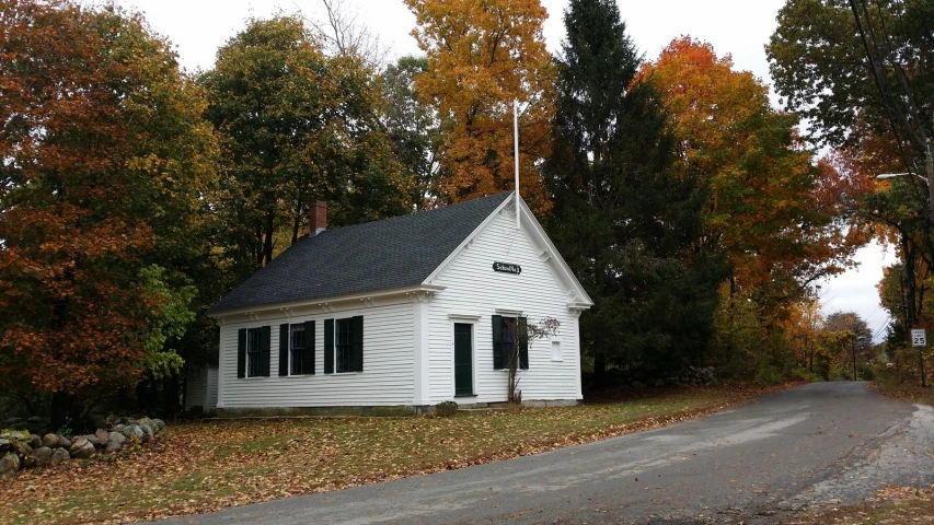 a small white house with black windows and a steeple near a street