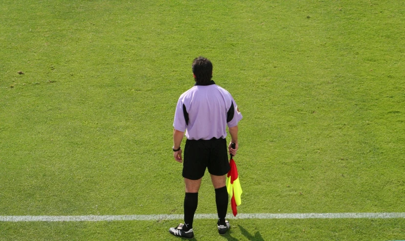 a referee standing on the sideline holding a yellow and red flag