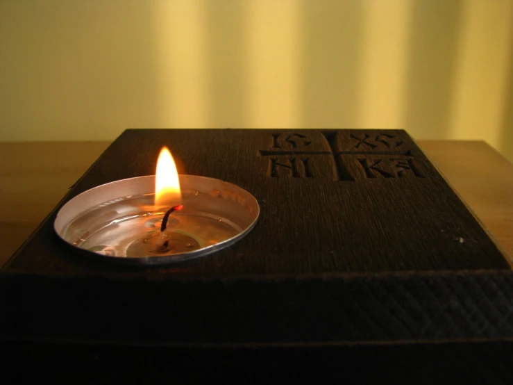 a lit candle on a metal container with writing on the inside