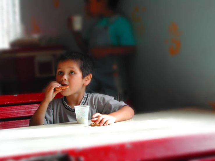 a boy eats his lunch and drinks out of a mug