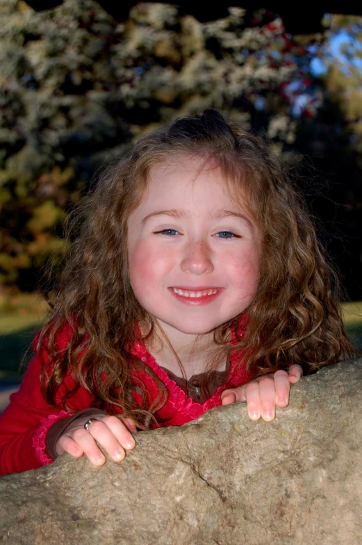 a little girl with long hair leaning on a large rock