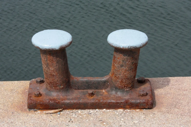 two rusty iron posts by a body of water