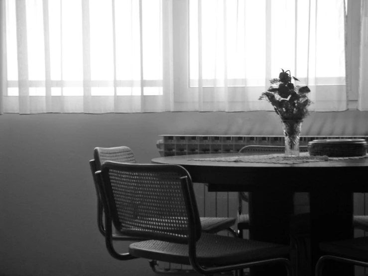 table with chairs and vase with flowers in it in front of window