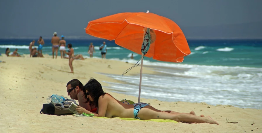 a man and woman laying on a beach under an umbrella