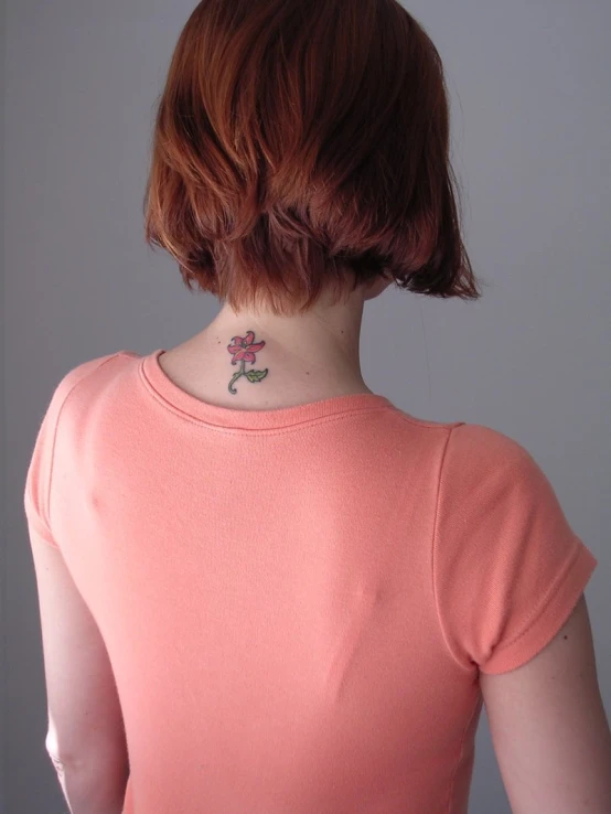 a woman with a pink shirt has a flower tattoo on her neck