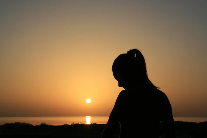 a person silhouetted at sunset looking towards the water