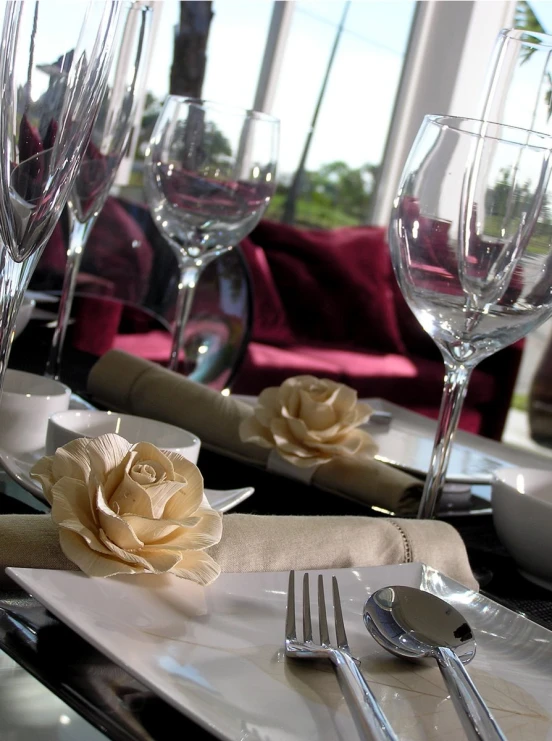 a place setting with glasses, napkins and rose on the table