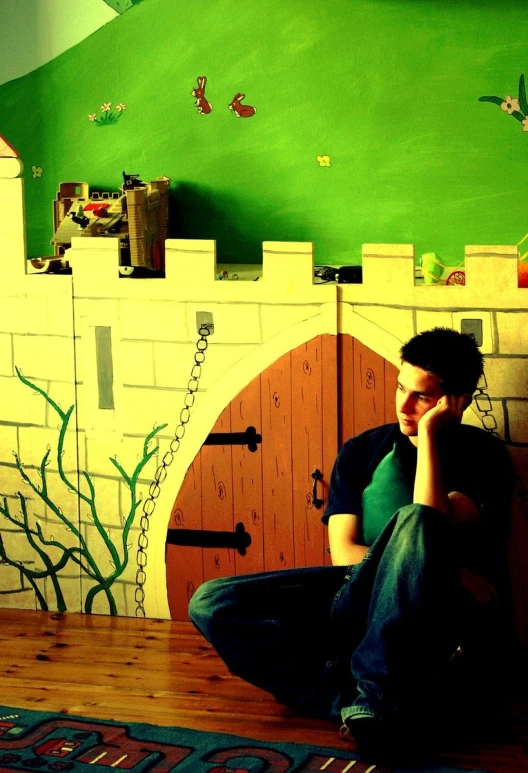 a boy sitting on a floor next to a fake white castle with walls and door