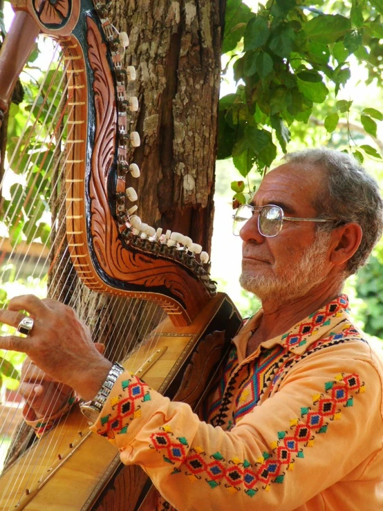 an old man plays a music instrument next to a tree