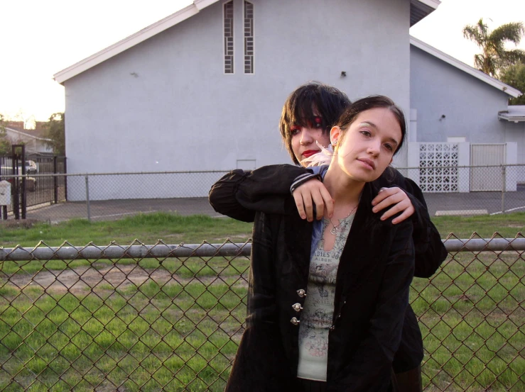 two young women, one of them leaning over the fence of a house