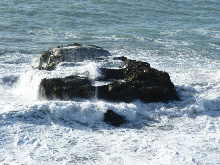 a large rock with rough surf coming into the ocean