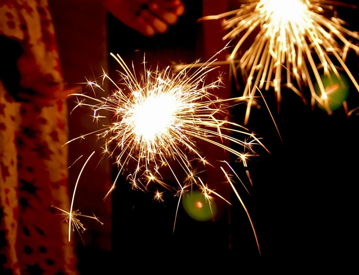 a girl is holding her hand near two sparklers