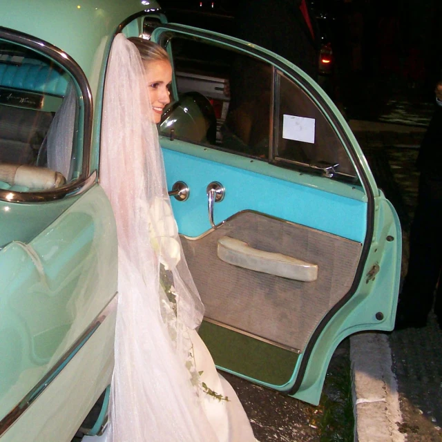 a beautiful woman standing next to a car wearing a bridal veil