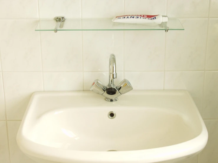 the corner of a sink with a glass shelf above it