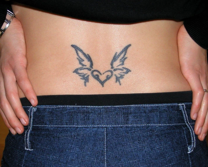 a person holding their stomach in front of the camera with a tattoo of two birds