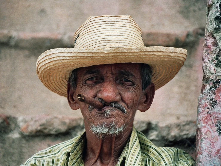 an older man wearing a straw hat standing with a cigarette