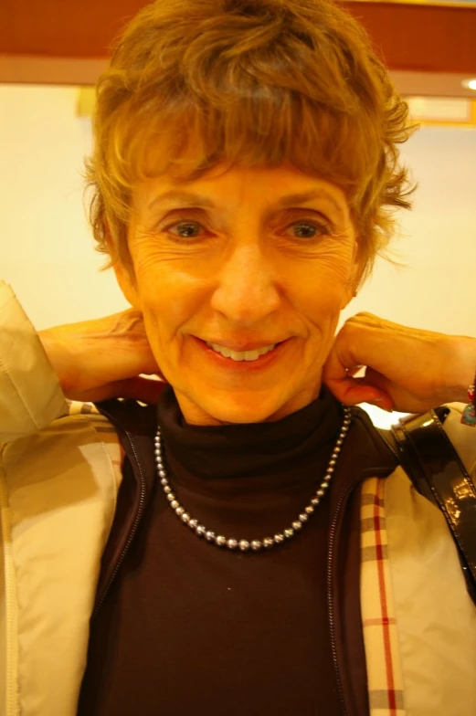 an older woman smiles wearing a necklace and jacket