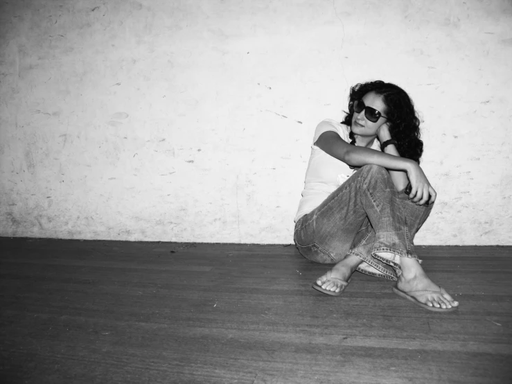 a girl with her hand on her face sitting in front of a wall