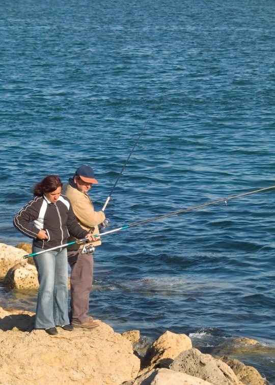 two people fishing on the rocks with one person holding soing in his hand