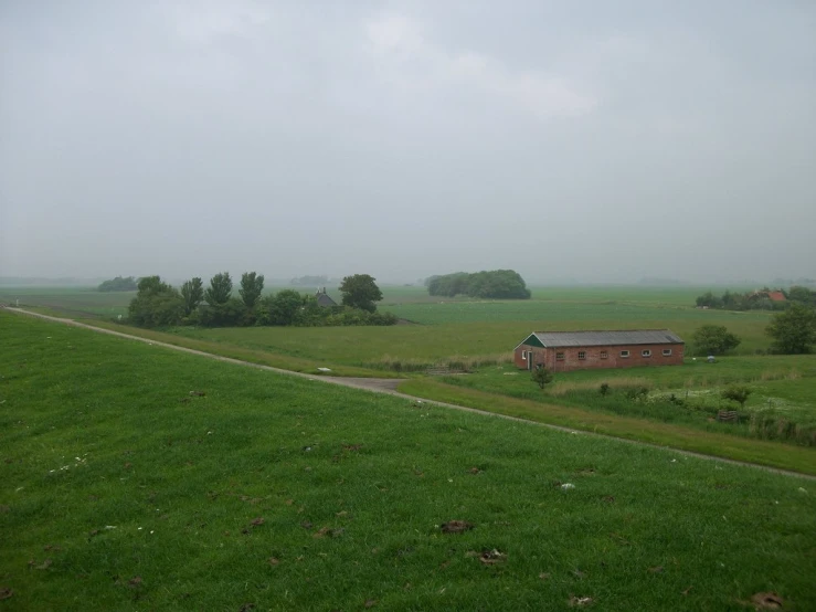 a grassy field with a dirt road and farm house