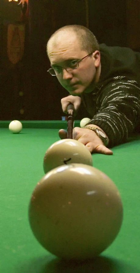 man leaning over a pool table with cues in his hand