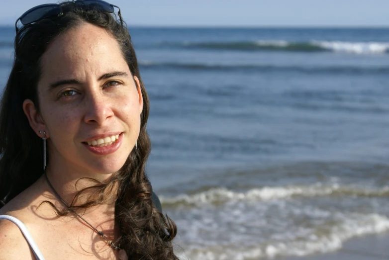 a woman smiles as she stands on the beach near the ocean