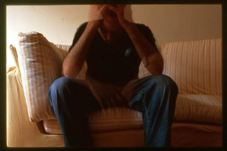 a man sits on top of a couch while covering his eyes