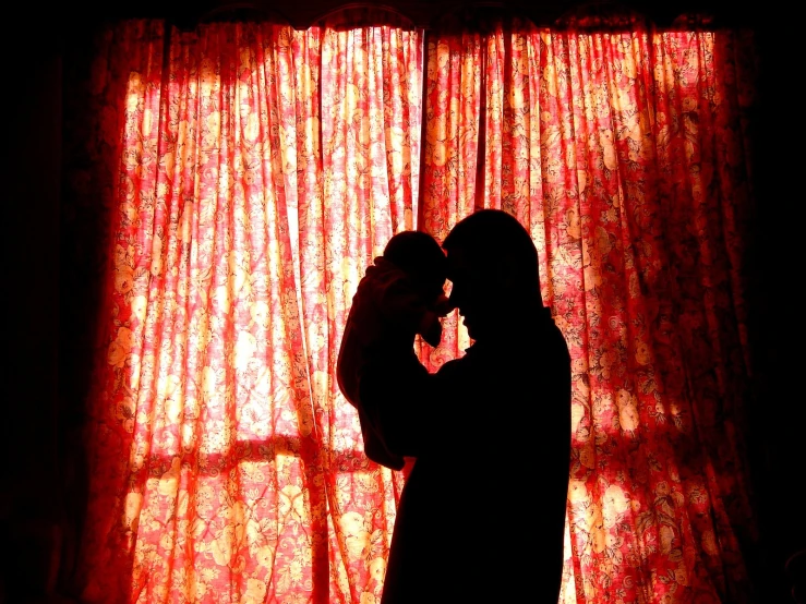 a man with a baby in his arms, standing next to a window