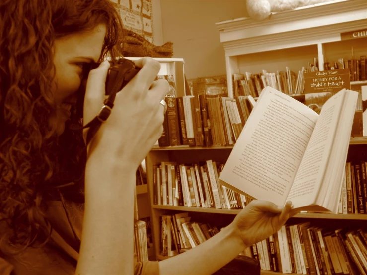 woman reading a book and holding a camera next to her head