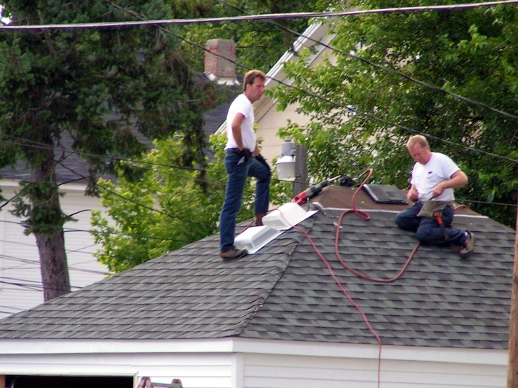 two men on top of a house fixing their roof