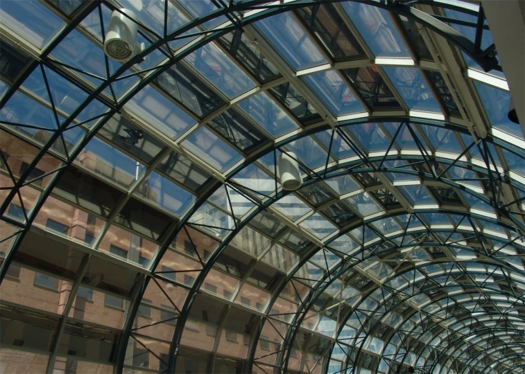 a building's glass roof with a clock at one side and two buildings on the other side