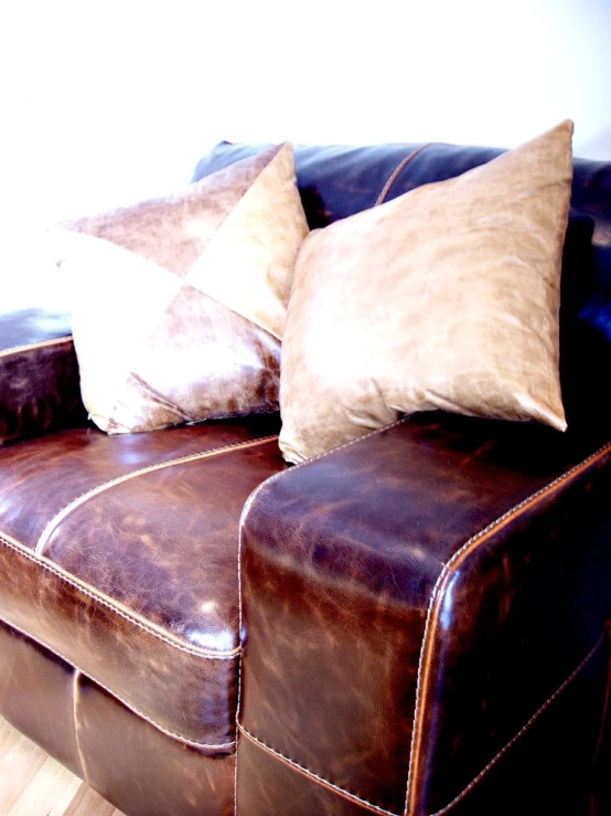 two brown and white pillows are on top of a brown leather couch