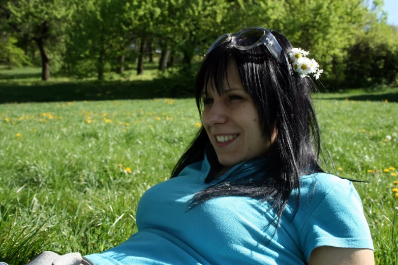 a smiling girl lying on the grass in front of a flower