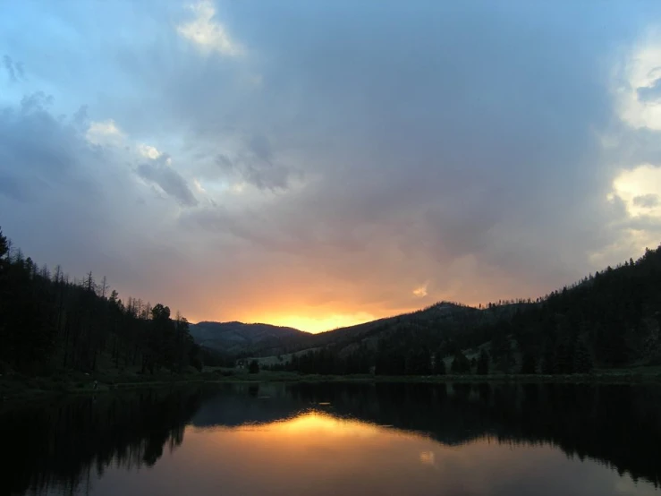 the setting sun behind a mountain reflecting in a lake