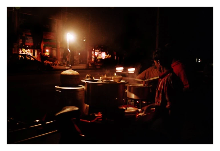 two men are cooking a large pot at a street side table