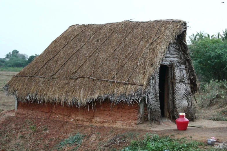 a grass hut with a straw roof and red water bucket