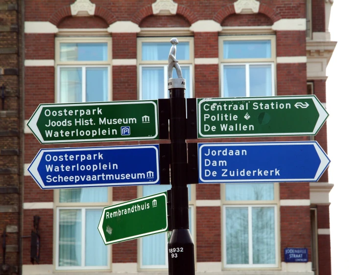 a tall green pole topped with lots of blue and white street signs