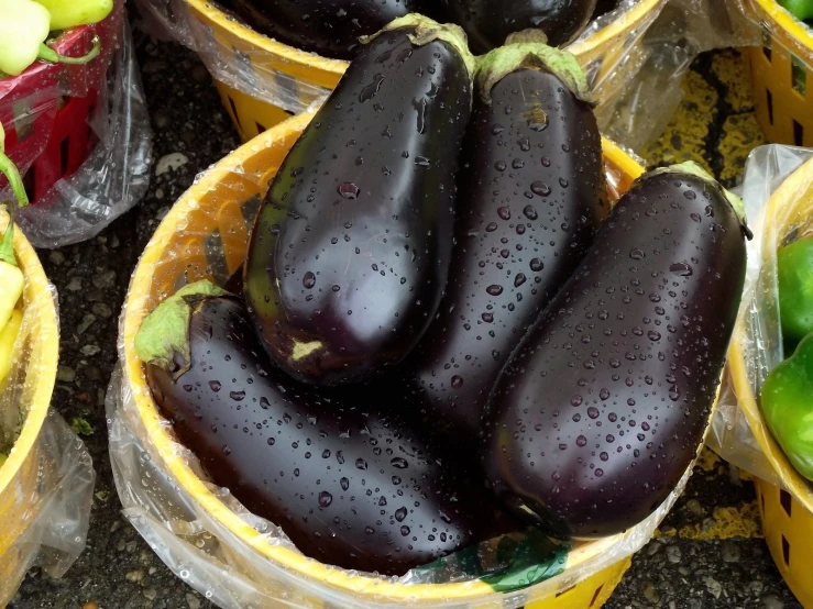 eggplant sits in baskets on the ground next to peppers