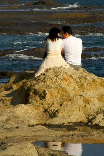 a man and a woman sit on top of a rock