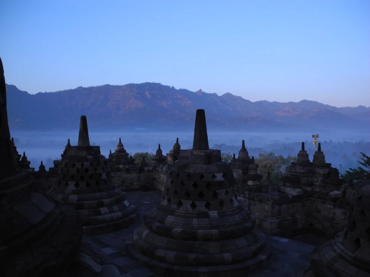 many buddhist buildings in an open area with mountains in the background