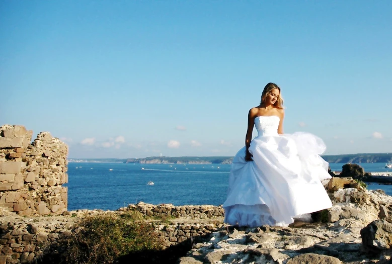 a bride walks down a rock ledge near the ocean