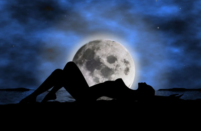 a woman is laying on a beach and looking at the moon
