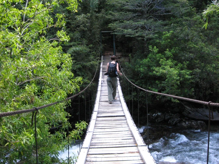 a man walking across a suspension bridge over a river