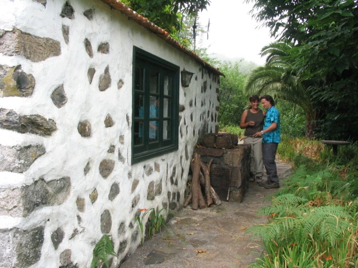 two people standing outside of a house next to a tree